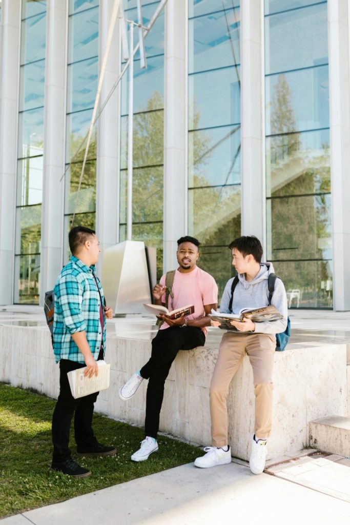 Three college students having a discussion outdoors near a modern campus building.